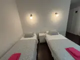 Cama individual con colcha gris y toalla rosa junto a una mesilla en la Habitación Doble Confort